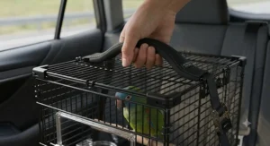 Hand holding the padded carrying handle of a portable collapsible bird travel cage